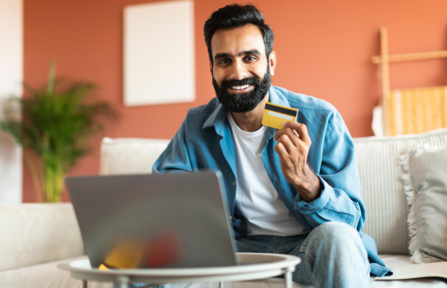 رجل يحمل بطاقة ائتمان ويتسوق جالسًا مع جهاز كمبيوتر محمول